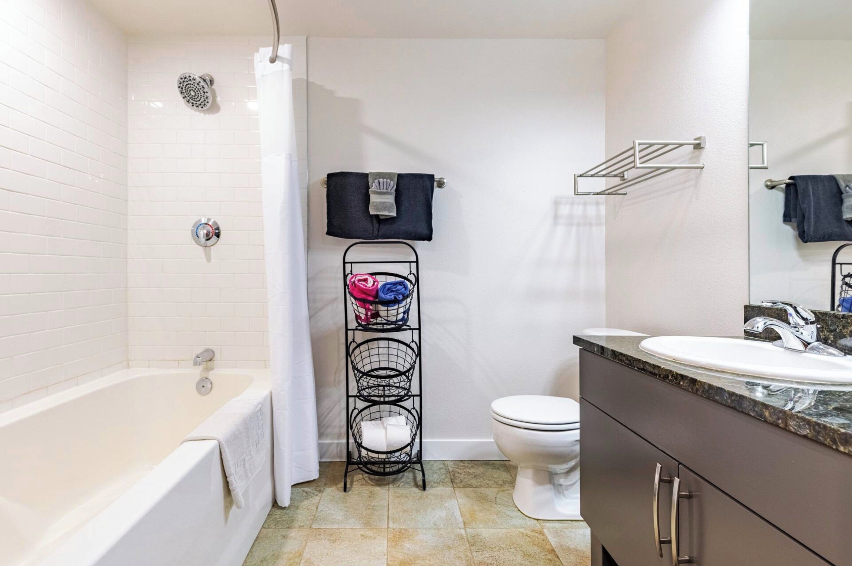 Un baño con bañera, inodoro y toallero con toallas dobladas.