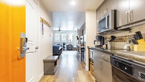 A narrow hallway with a kitchen on one side, a dining area with a table and chairs, and a living room with a sofa and a TV. - Newly Remodeled Studio steps from the lifts of Winter Park Base (Winter Park)