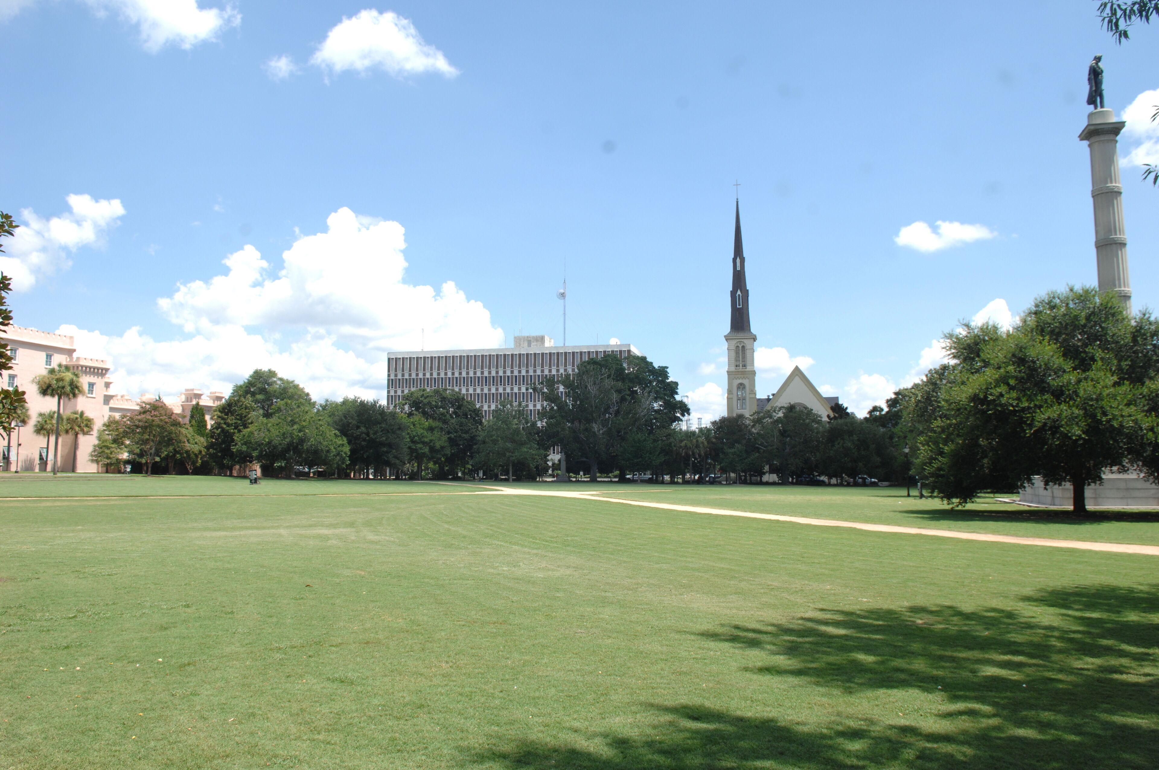 A large open grassy field with a tall building and a church in the background.