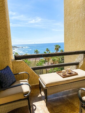 A balcony with a view of the ocean, a wicker table with a tray, and a cushioned chair. - Overlook the Sea of Cortez & Pool in Spacious living area (Cabo San Lucas)