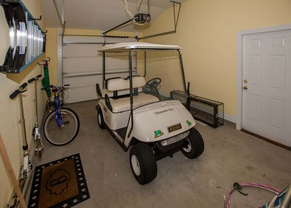 Un garaje con un carrito de golf identificado con 'Vitamin Sea' y una bicicleta.