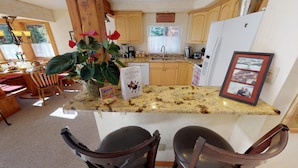 A kitchen with wooden cabinets, a granite countertop, a refrigerator, and a dining area with chairs and a table.