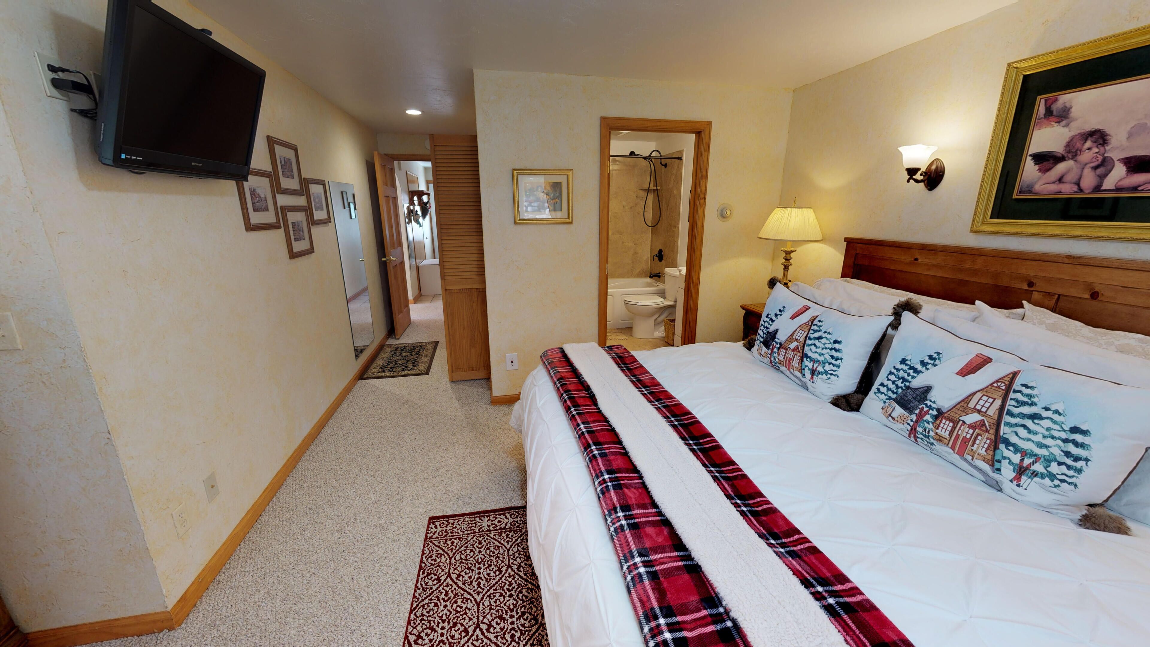 A hotel room with a bed, a television, a bathroom, and a hallway.