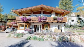 A chalet-style building with a wooden balcony, flower boxes, and a stone pathway leading to the entrance.