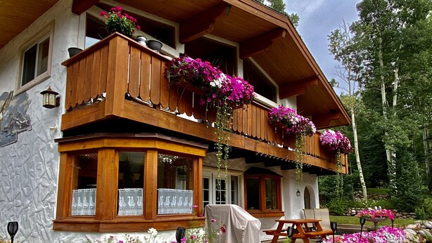 A traditional chalet with wooden balconies, a stone facade, and a garden with colorful flowers.