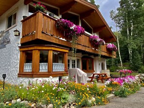 Un chalet traditionnel doté de balcons en bois, d’une façade en pierre et d’un jardin aux fleurs multicolores.