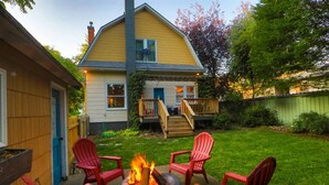 Un patio trasero con un brasero, sillas Adirondack rojas y una casa con terraza.