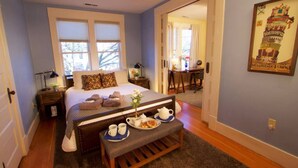 Un dormitorio con cama, mesitas de noche, un banco con una bandeja de desayuno y una puerta que da a otra habitación.