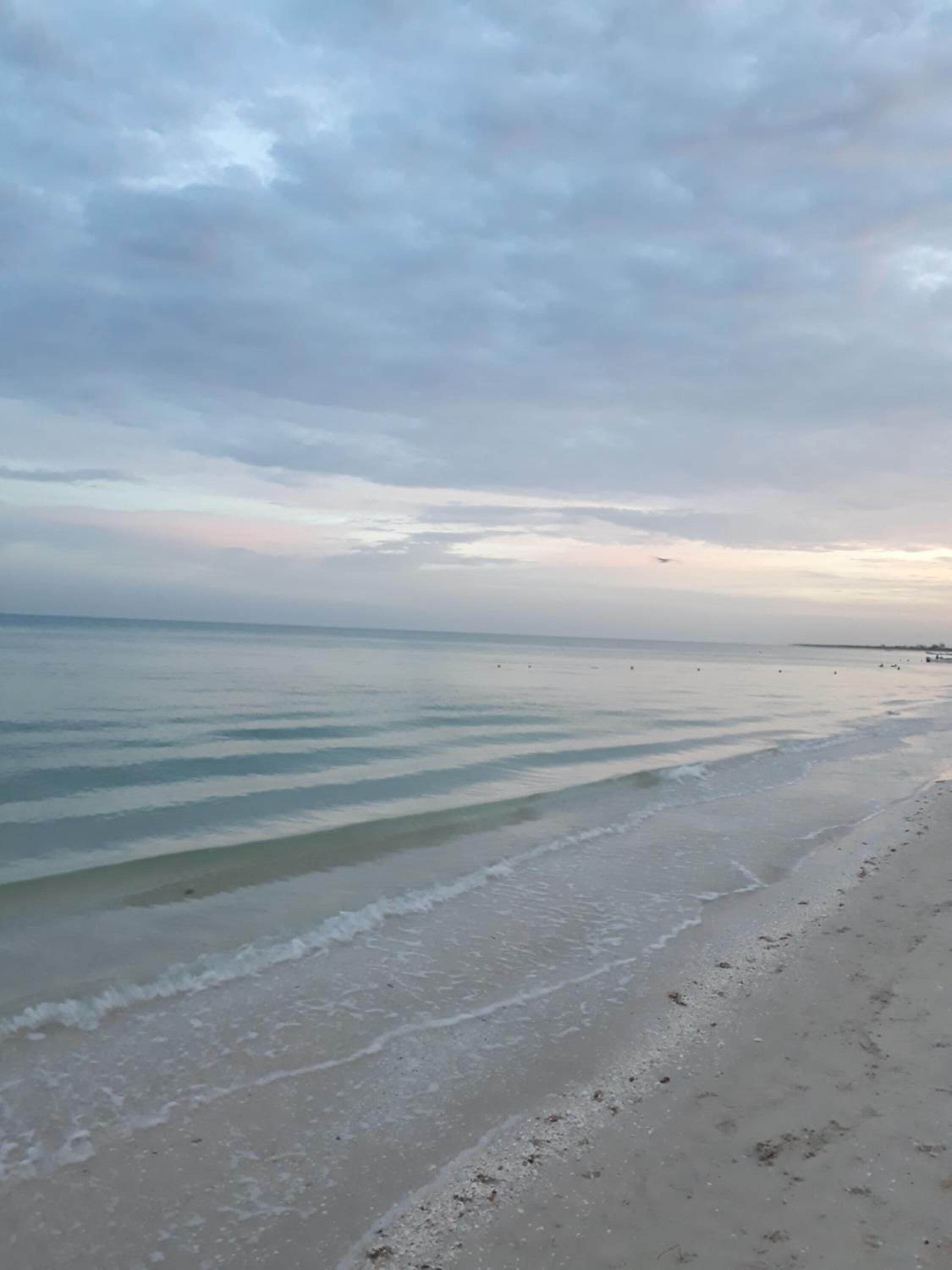 Een strand met rustig water en een bewolkte lucht.