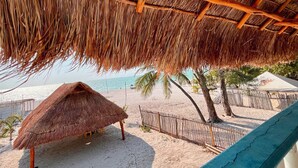 A beach scene with a thatched roof structure, palm trees, and a sandy beach. - Posada Maria Isabel (Celestún)