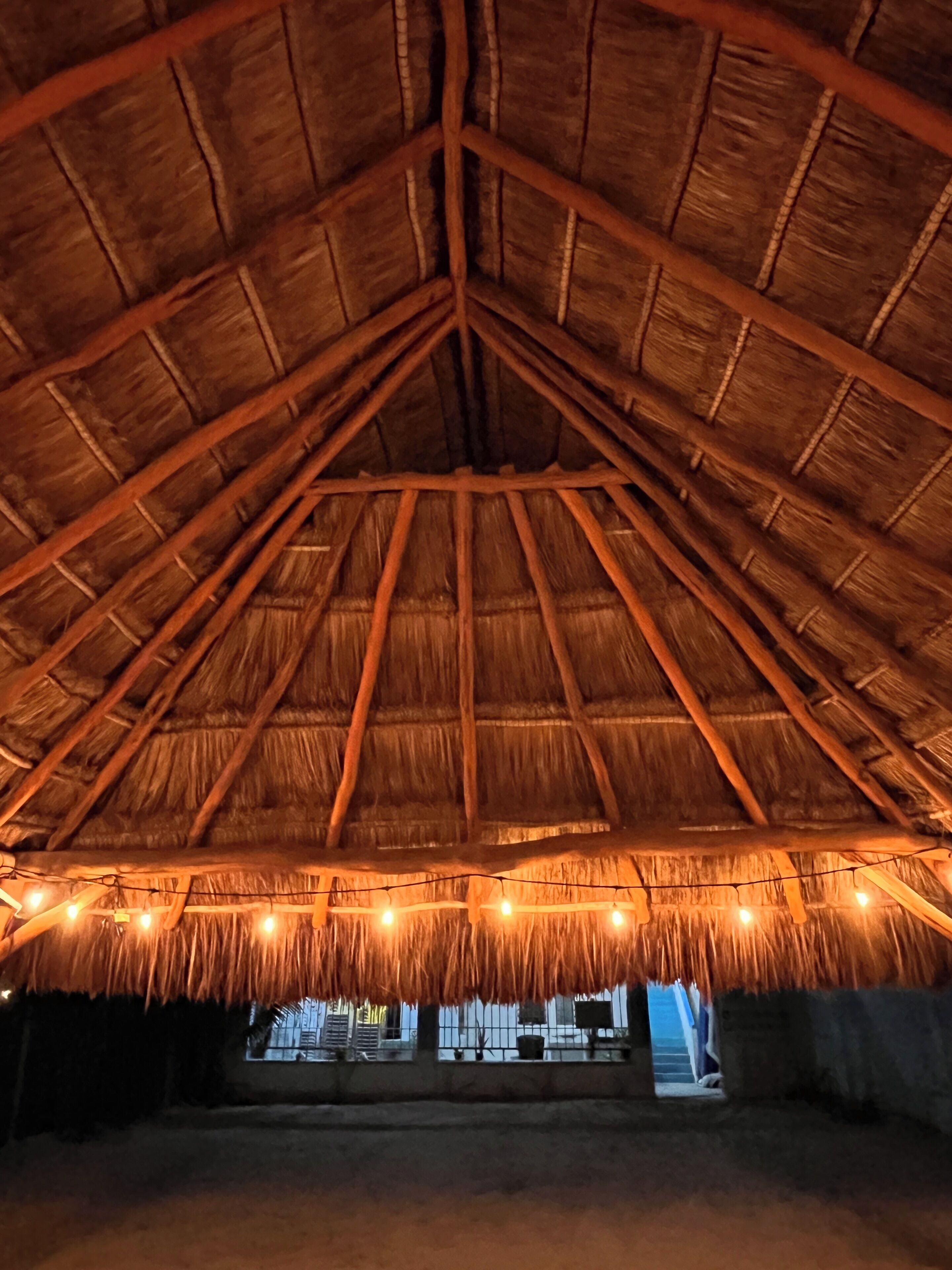 Una estructura con techo de paja y diseño central de viga de madera, adornada con luces colgantes.