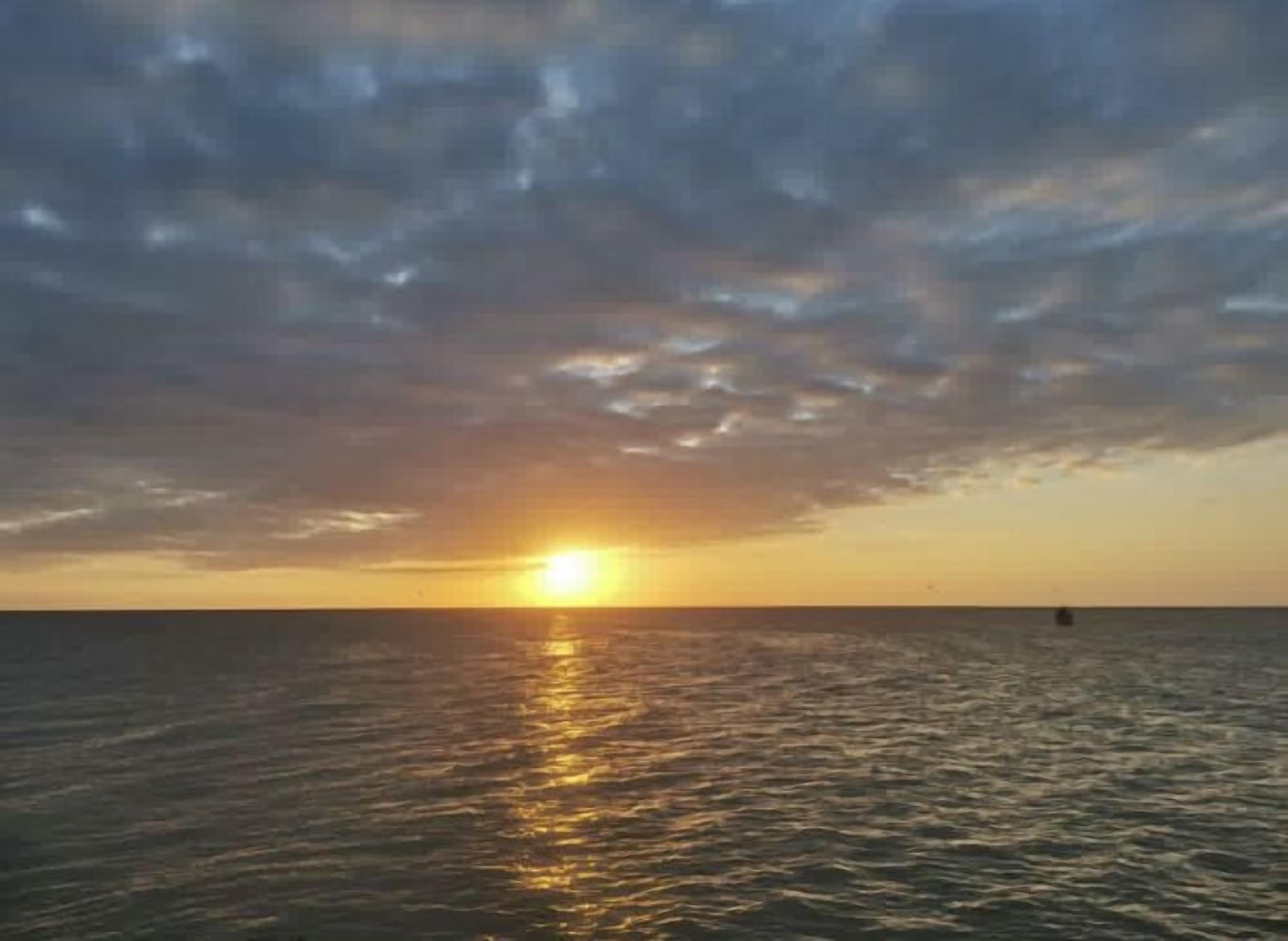 Un coucher de soleil sur une mer calme, avec un bateau à l'horizon.