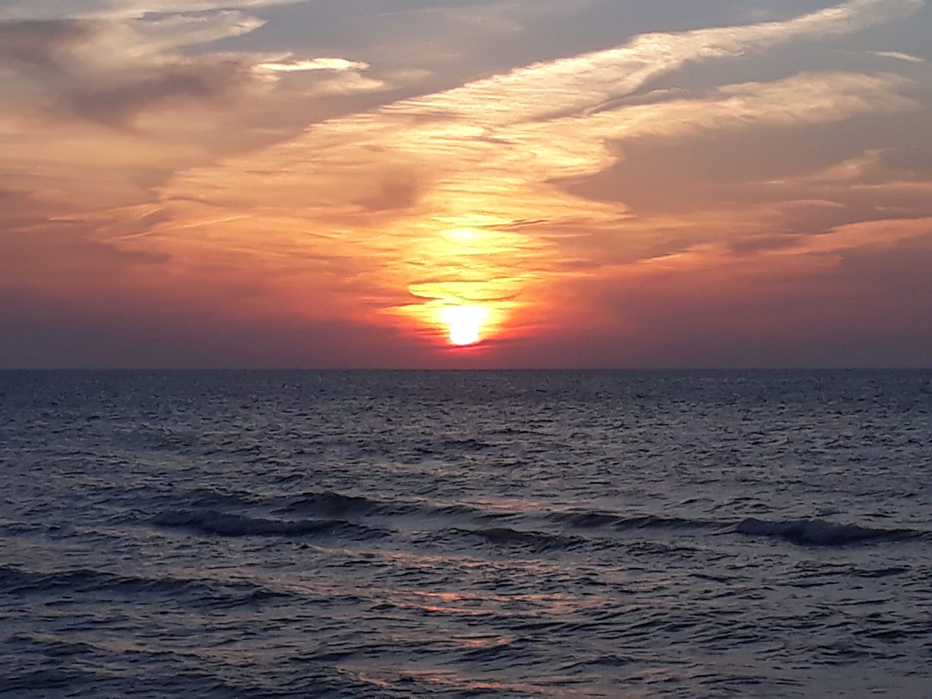 Ein Sonnenuntergang über dem Meer mit Wellen im Vordergrund.