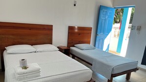 A room with two beds, one larger and one smaller, both with wooden headboards and white linens. A roll of toilet paper and a stack of towels are on the larger bed. - Posada Maria Isabel (Celestún)