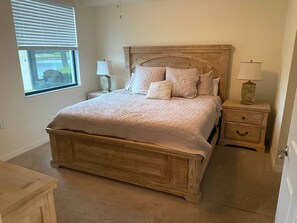 A bedroom with a wooden bed, two bedside tables with lamps, a window with blinds, and a door.