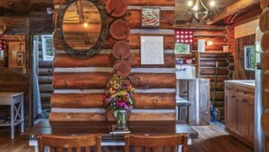 Un interior rústico de madera con un comedor que incluye dos sillas de madera, un espejo y un florero con flores.