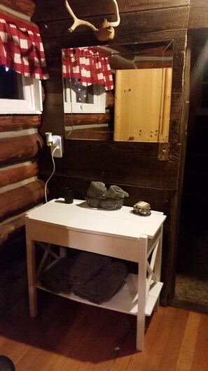 Interior rústico de una cabaña de madera, con una mesa blanca, cortina a cuadros rojos y blancos, y un armario de madera.