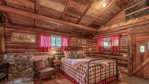 Una habitación tipo cabaña de troncos con pared de piedra, una cama de madera, una silla y una mesita de noche.