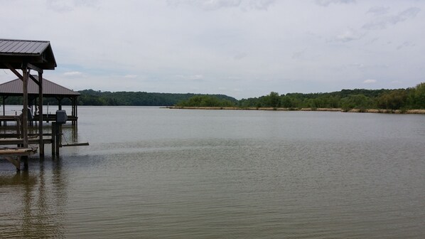 A wooden pier extending into calm water, surrounded by trees and hills.