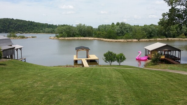 Een vakantiehuis aan het meer met een houten steiger, een tuinhuisje en een roze flamingo die drijft.
