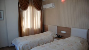 Habitación de hotel con dos camas, cabecero, unidad de aire acondicionado y mesita de noche con teléfono.
