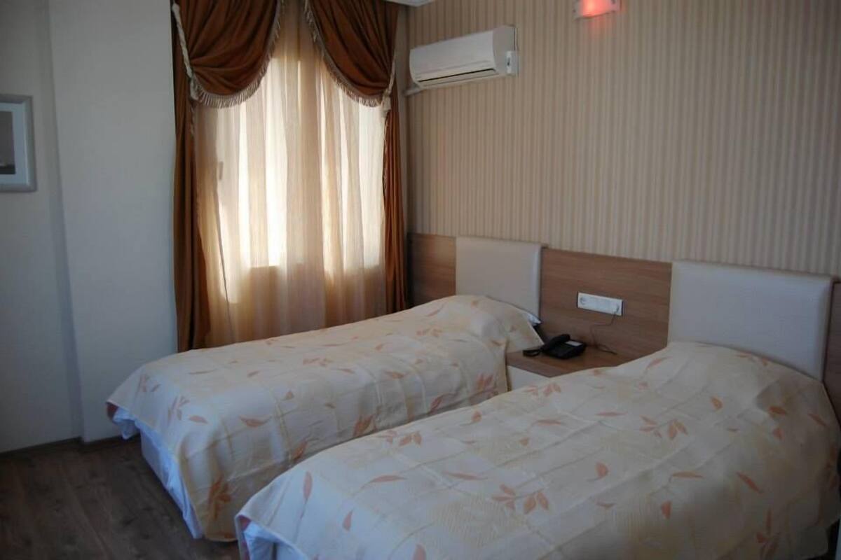 A hotel room with two beds, a headboard, an air conditioning unit, and a nightstand with a phone.