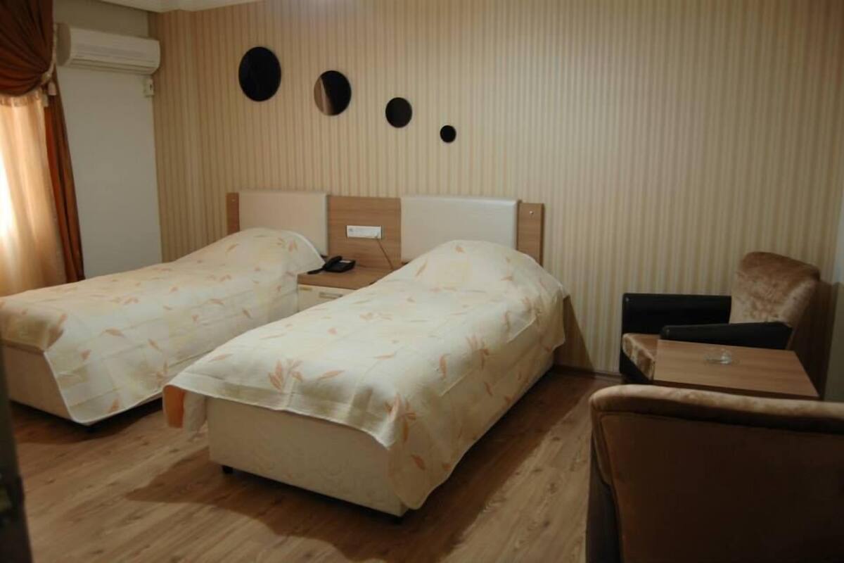A hotel room with two single beds, a small table, a chair, and a wall-mounted TV.