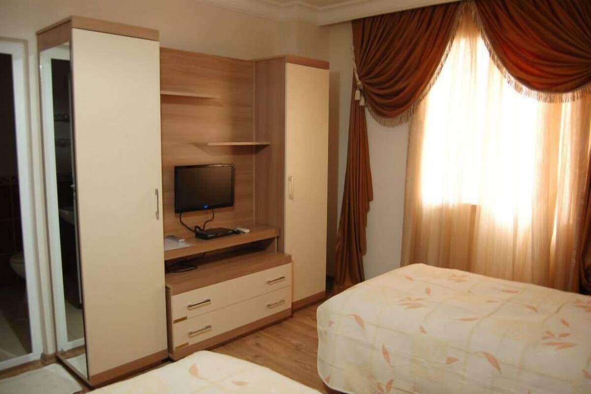 A bedroom with a bed, a TV on a wooden stand, and a wardrobe.