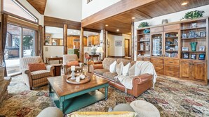 A spacious living room with a high ceiling, wooden beams, a large window, and a cozy seating area with a coffee table.