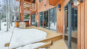 A wooden cabin with large glass doors and windows, a stone fireplace, and a wooden deck.