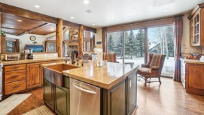 A spacious kitchen with a large island, wooden cabinets, and a view of a snowy landscape through large windows.