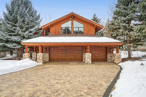 Ein zweistöckiges Holzhaus mit großer Garage, Steinpfeilern und einem mit Schnee bedeckten Dach.