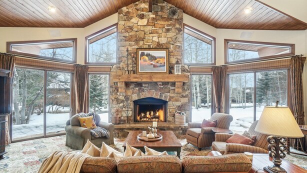A cozy living room with a stone fireplace, large windows, and a high ceiling.