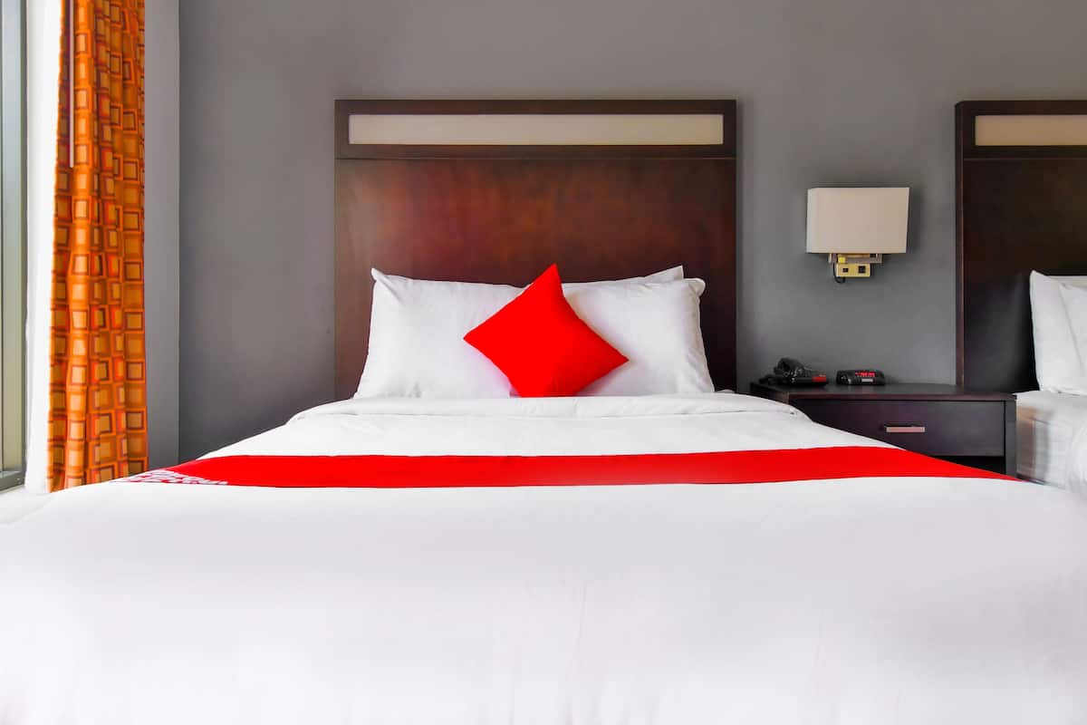 A hotel room with a large bed, a wooden headboard, a bedside table with a lamp, and a window with curtains.