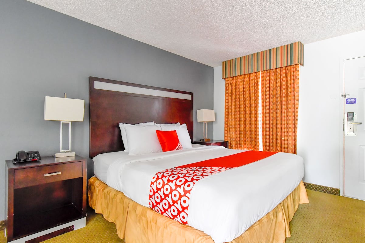 A hotel room with a large bed, two bedside tables, a nightstand, and a door with a sign.