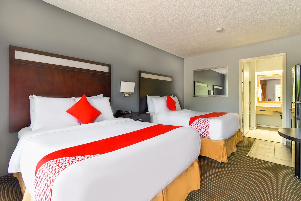 A hotel room with two beds, a wooden headboard, a nightstand, a mirror, and a bathroom visible through an open door.