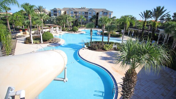 A resort pool area with a water slide, palm trees, and a building in the background. - Family Paradise w/ Pvt Pool, BBQ Grill, Themed Bedrooms, Game Room & Club access (Kissimmee)