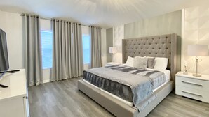A modern bedroom with a tufted headboard, a large bed, a bedside table with a lamp, and a television on a stand. - Family Paradise w/ Pvt Pool, BBQ Grill, Themed Bedrooms, Game Room & Club access (Kissimmee)