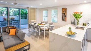A modern kitchen with a white countertop, a dining area with a table and chairs, and a sofa with cushions. - Villa Del Mar - Beachfront Port Douglas (Port Douglas)
