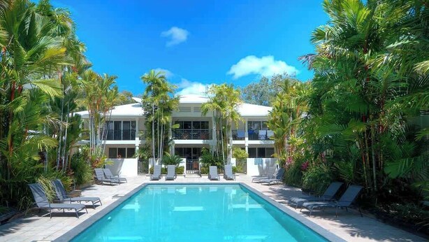 A poolside view of a resort with a clear blue pool, lounge chairs, and palm trees. - Villa Del Mar - Beachfront Port Douglas (Port Douglas)