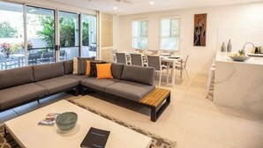 A modern living room with a sectional sofa, a coffee table, and a dining area with a table and chairs. - Villa Del Mar - Beachfront Port Douglas (Port Douglas)