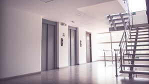 A modern elevator area with three elevators, a staircase, and a clear view of the outside. - Family_ friendly (Cuenca)