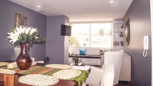 A modern living room with a dining area, a large window with a city view, and a flat-screen TV mounted on the wall. - Family_ friendly (Cuenca)