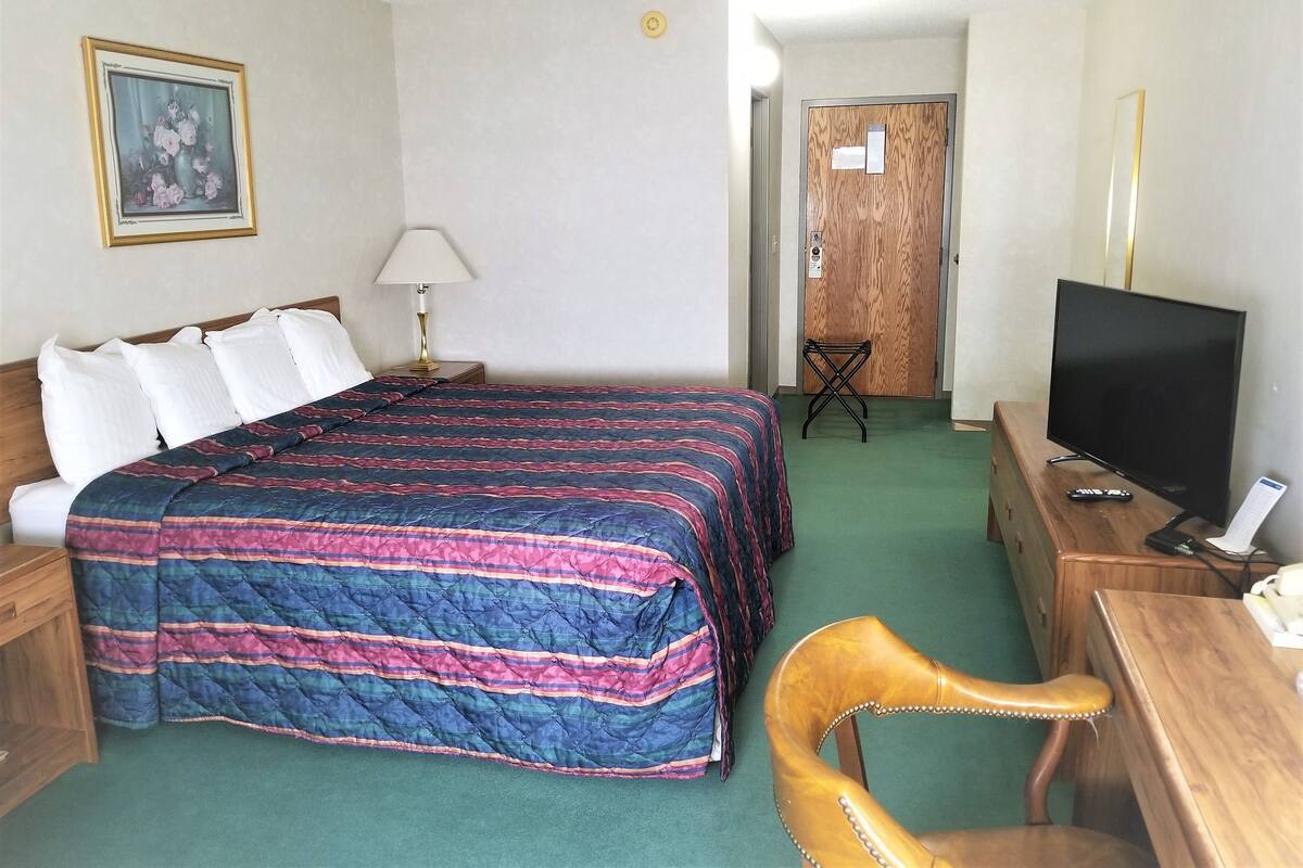 A hotel room with a bed, a desk, a television, a chair, a lamp, and a door.