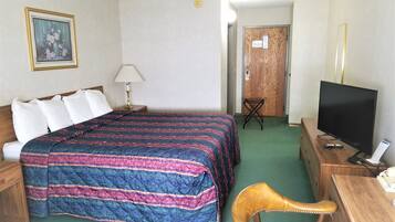 Ett hotellrum med en säng, ett skrivbord, en tv, en stol, en lampa och en dörr.