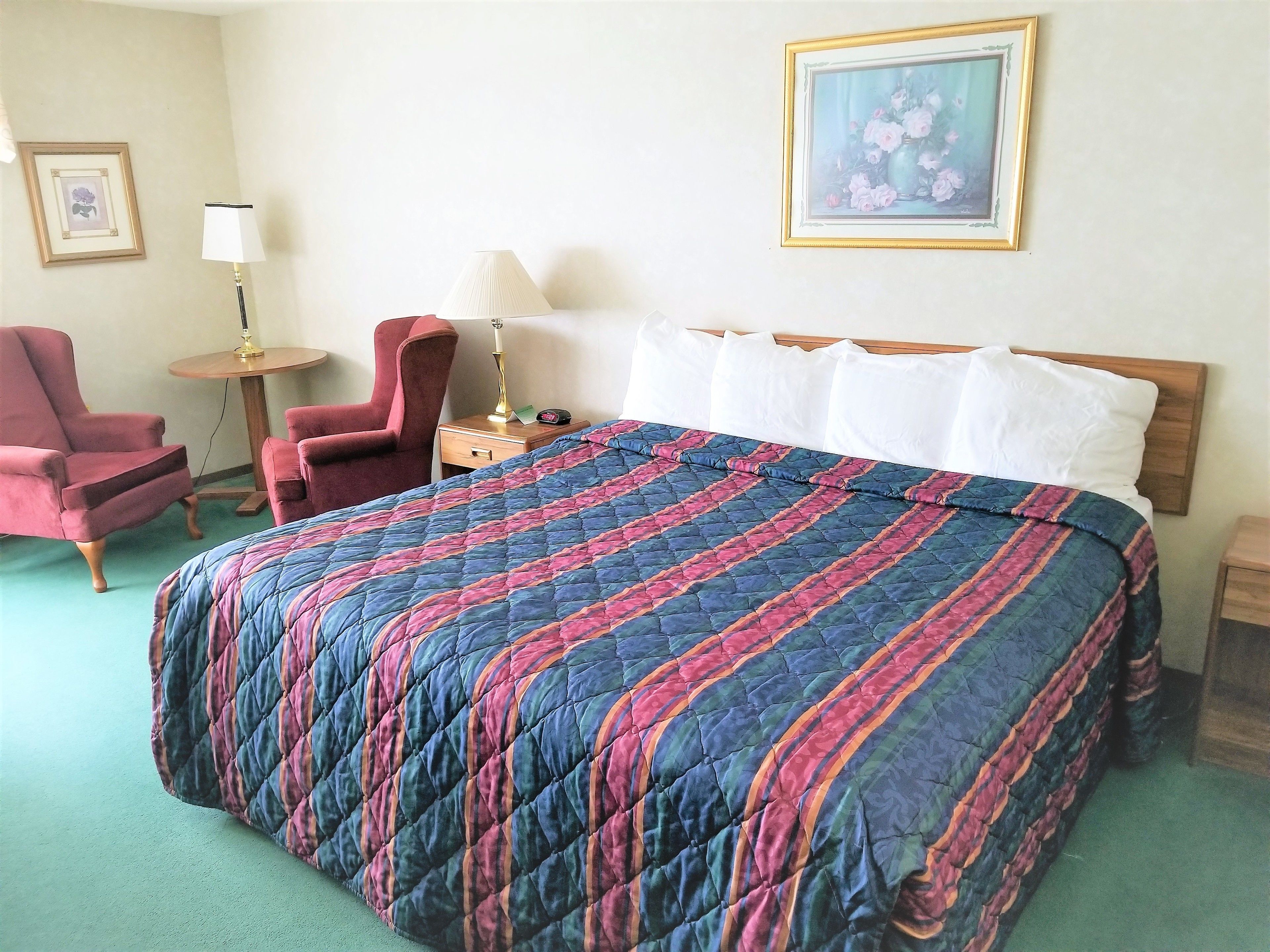 Una habitación de hotel con una cama grande, dos sillones, una mesita de noche con una lámpara y un cuadro enmarcado en la pared.