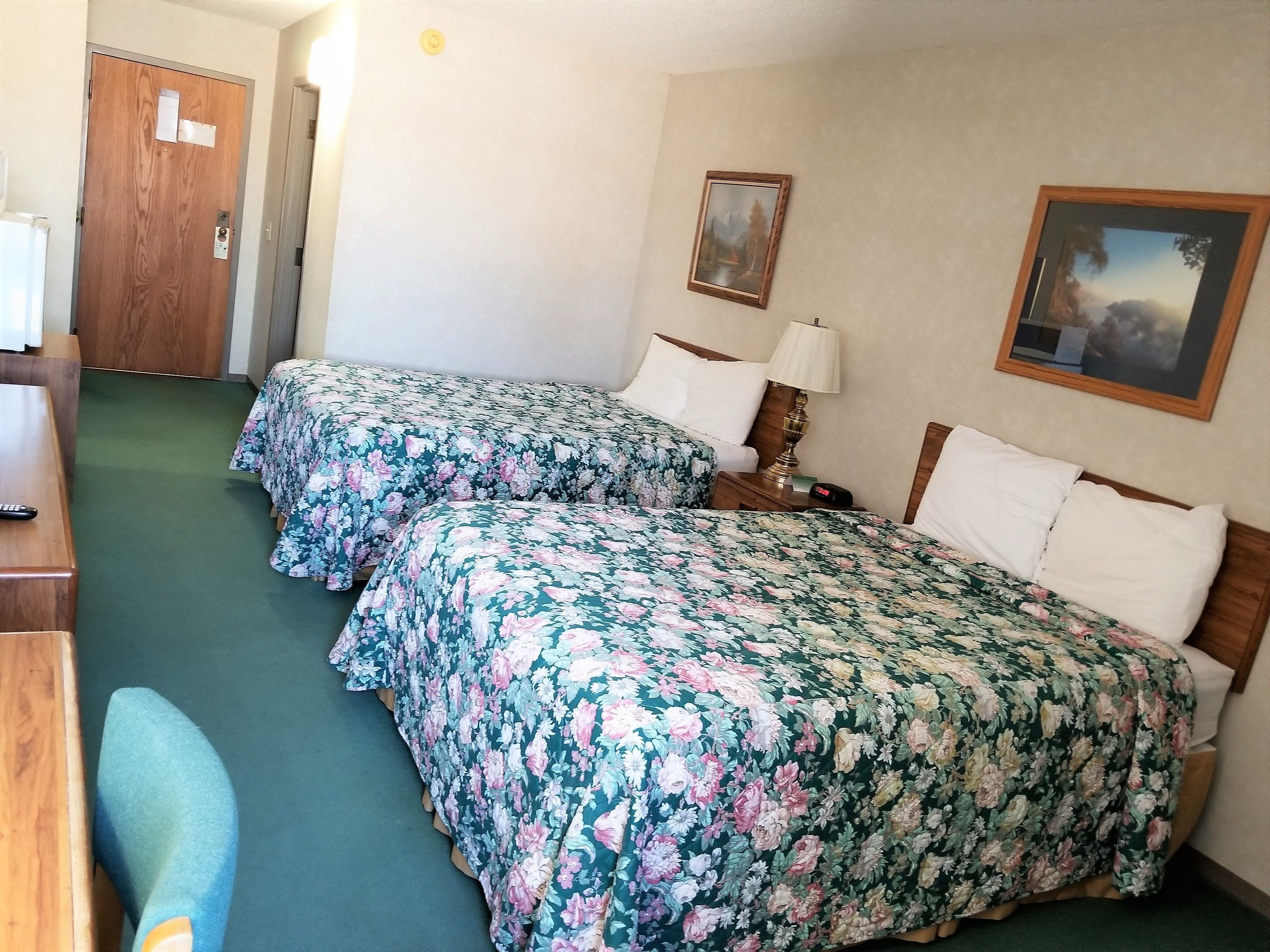 A hotel room with two beds, a desk, a chair, a lamp, and a painting on the wall.