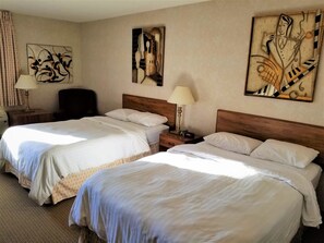 A hotel room with two beds, a wooden headboard, a nightstand with a lamp, and abstract wall art.