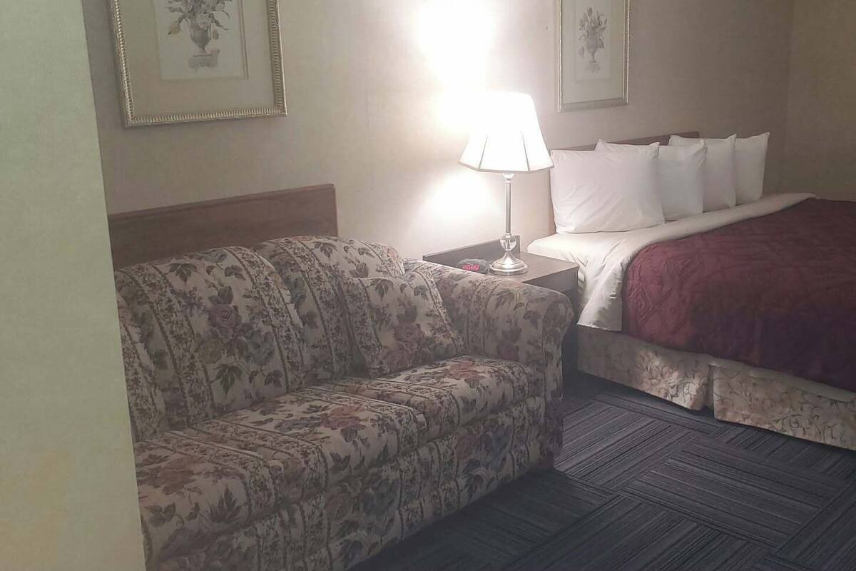 A hotel room with a bed, a sofa, a lamp, and two framed pictures on the wall.