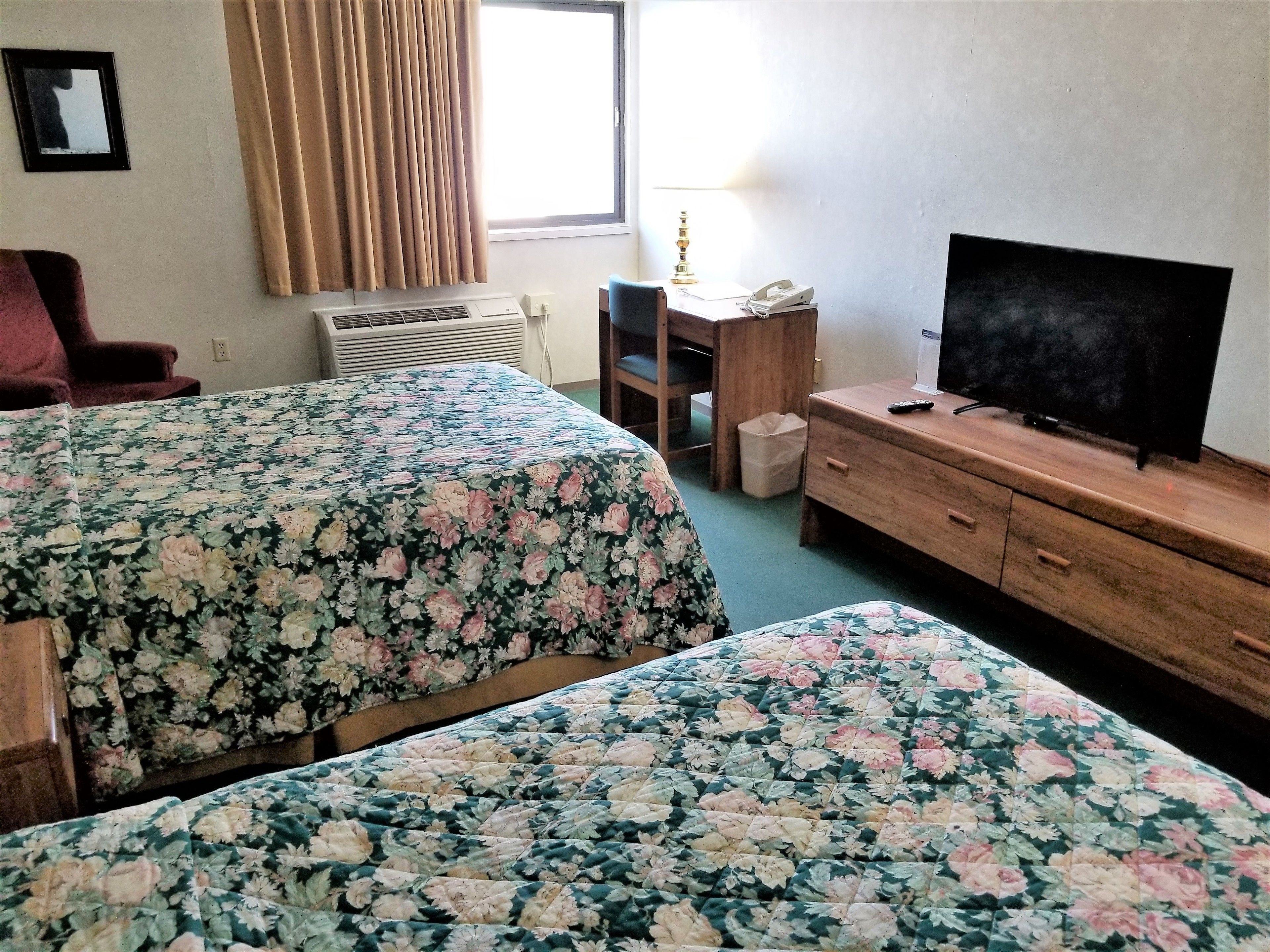A hotel room with two beds, a TV, a desk, and a window with curtains.